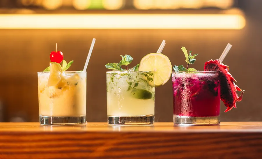 Drei bunte Signature Cocktails mit Kirsche, Limette und Drachenfrucht nebeneinander auf der Bar